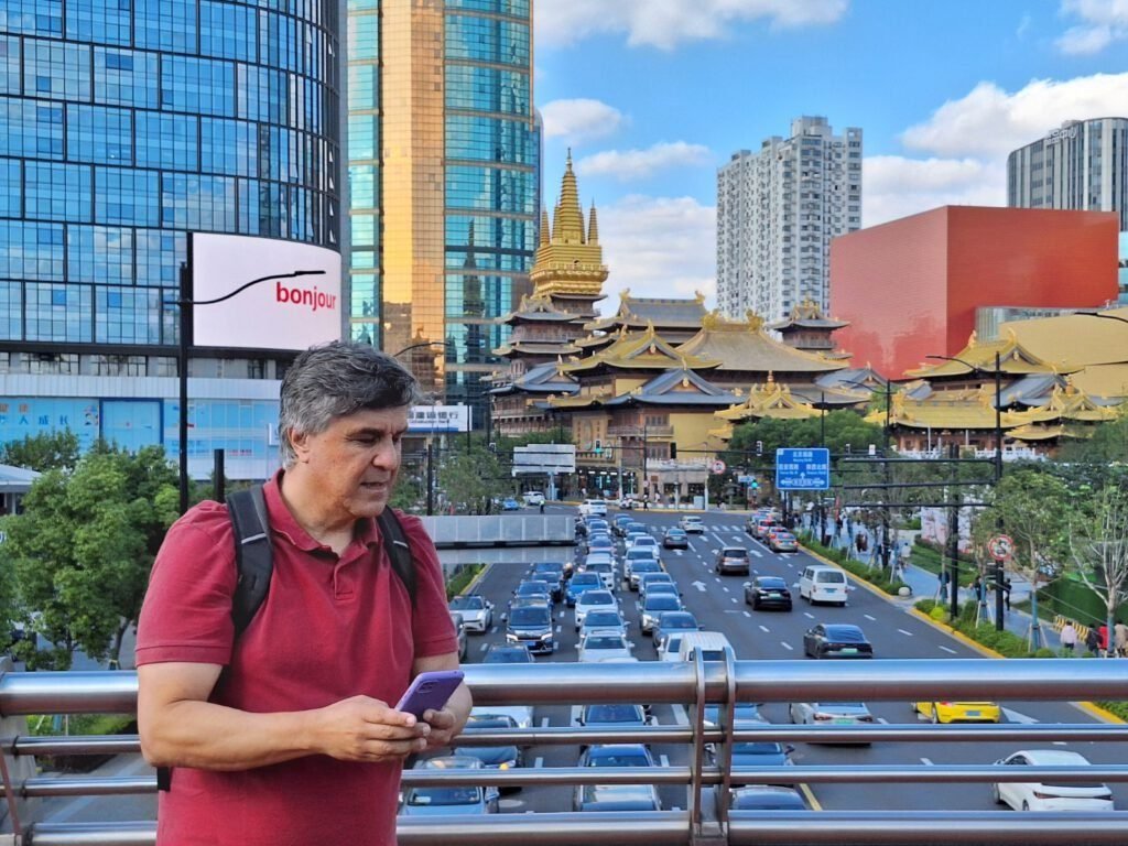 Espártaco da Rocha Dutra em uma passarela sobre uma avenida em Shanghai, com um templo tradicional e arranha-céus ao fundo.